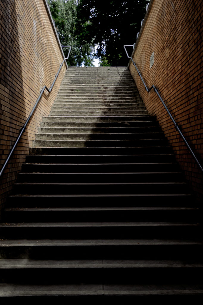 A flight of concrete steps rises between brick walls at Platform 17 in Berlin. Light falls across the stairway, dividing shadow from brightness. This quiet exit stands above the tracks from which thousands of Jewish men, women, and children were deported during the Second World War.